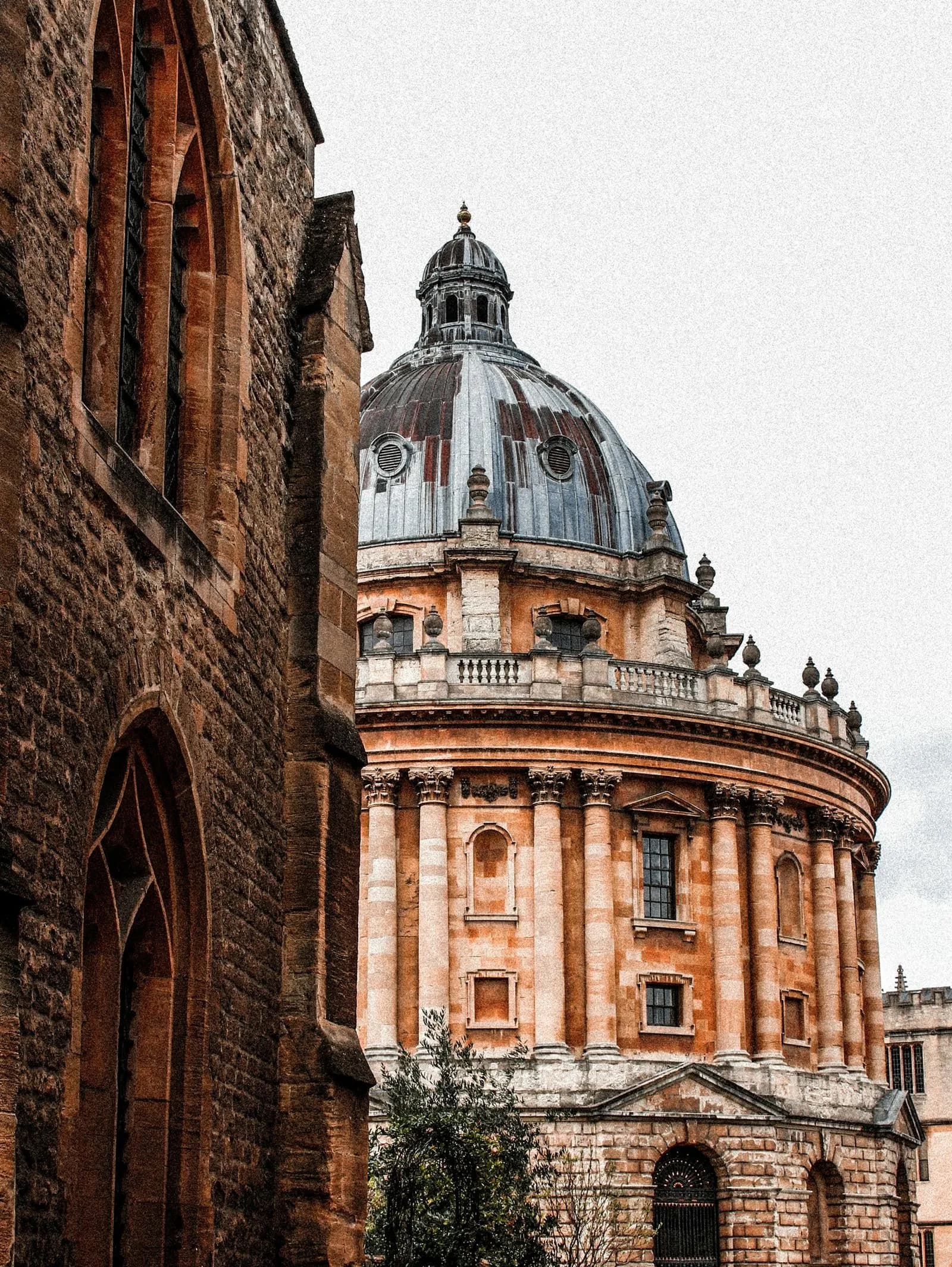 A vertical, architectural photograph of the Radcliffe Camera in Oxford, UK, seen from a narrow perspective.